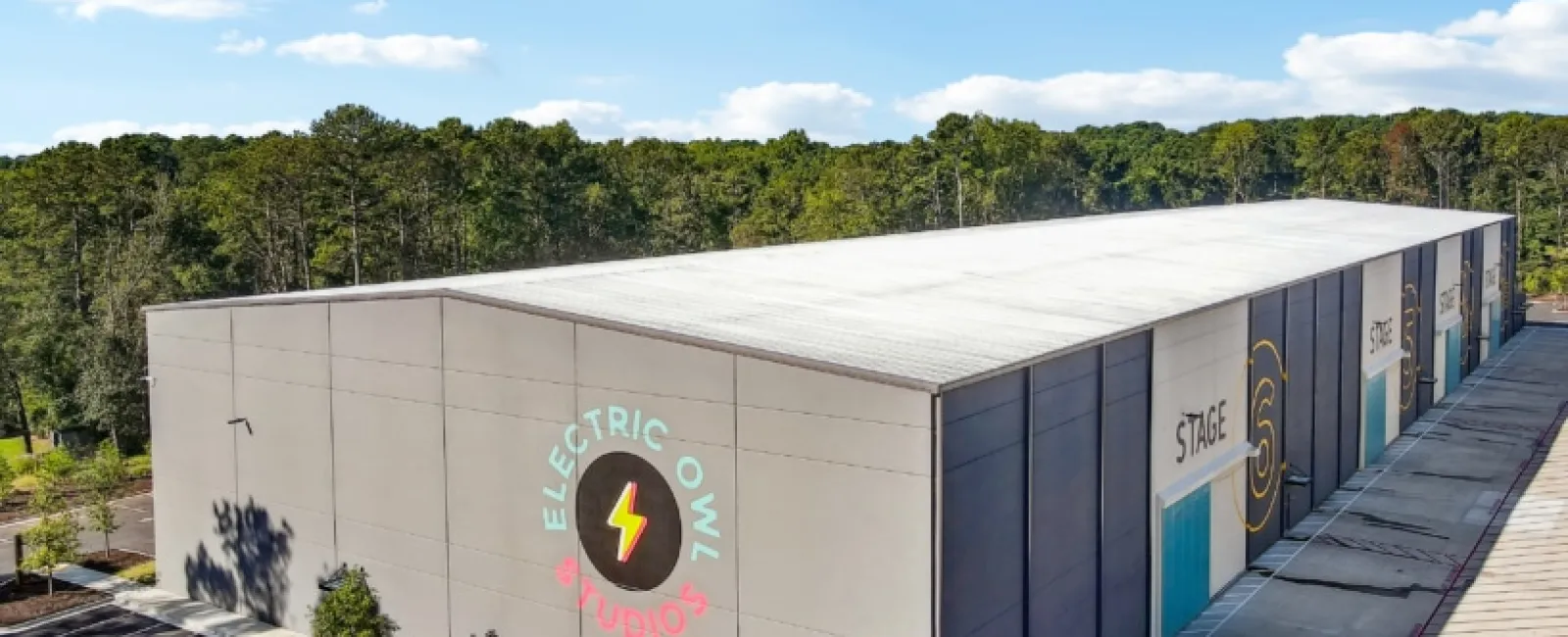 Modern large gray studio building with Electric Owl Studios logo and multiple stages under clear blue sky.