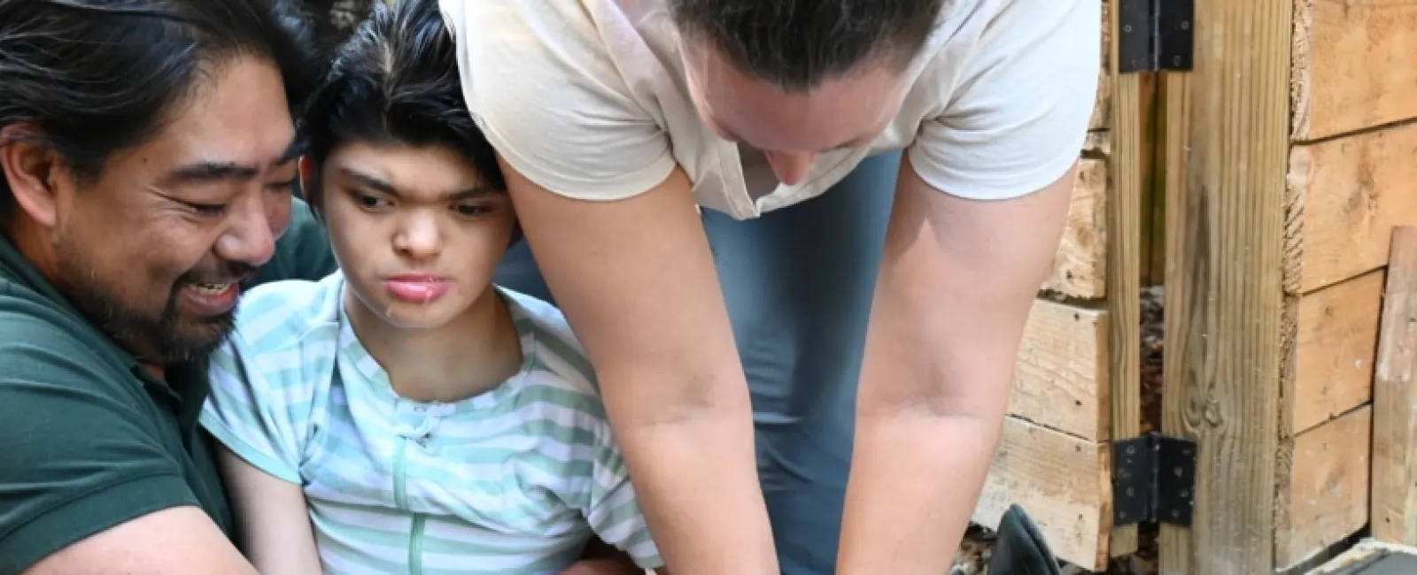 Family placing hands together to press on freshly poured concrete in a wooden frame outdoors.