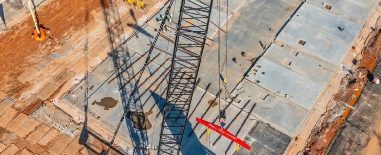 Aerial view of construction site with crane lifting concrete slab and workers managing placement