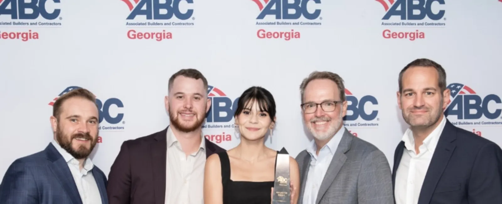 Group of five professionals posing with an award at the ABC Georgia event backdrop.