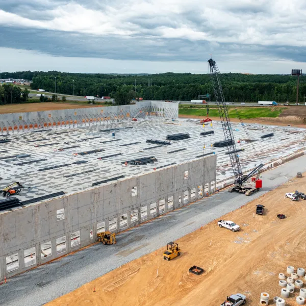Aerial view of large industrial building under construction with cranes, vehicles, and concrete walls on a cloudy day