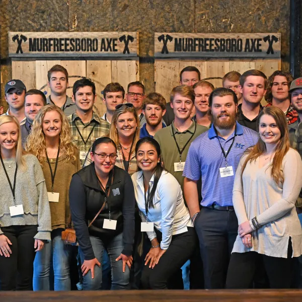 Group of young adults posing inside Murfreesboro Axe with wooden axe targets in background