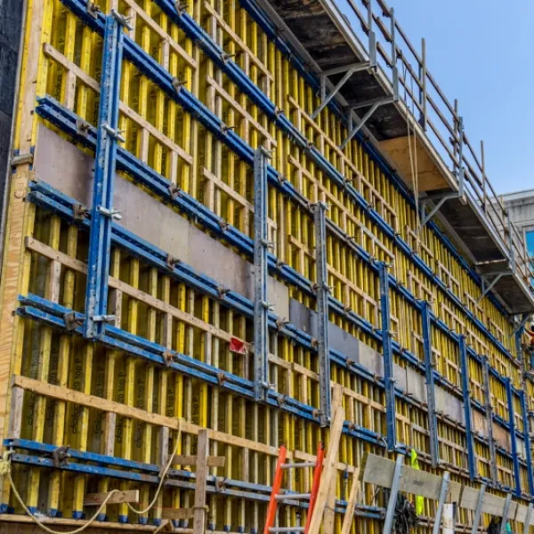 Large yellow and blue concrete formwork installed on a construction site with workers and scaffolding nearby.
