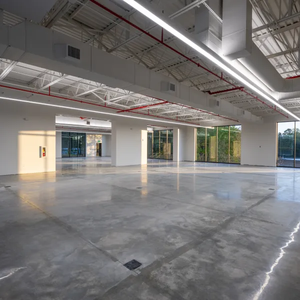 Empty modern commercial space with polished concrete floors, large windows, and exposed ceiling beams.