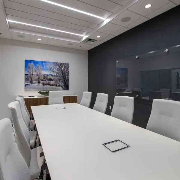 Modern office conference room with white table, comfortable chairs, and artwork on the wall under recessed lighting