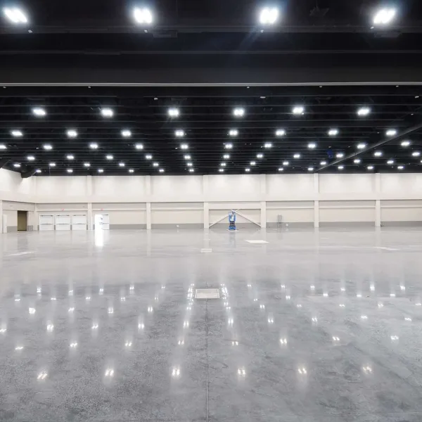 Spacious empty industrial warehouse with polished concrete floor and rows of ceiling lights reflecting on the surface