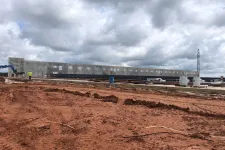 Thumbnail for Construction site with large concrete wall panels being erected under cloudy sky on red dirt ground.