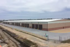 Thumbnail for Large industrial warehouse with multiple loading docks and a fenced perimeter under a cloudy sky.