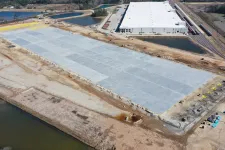 Thumbnail for Aerial view of large warehouse construction site with concrete foundation and surrounding water bodies in a rural area.