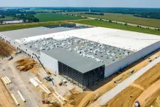 Thumbnail for Aerial view of a large warehouse under construction surrounded by farmland and construction equipment.