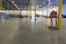 Thumbnail for Spacious industrial warehouse interior with yellow support beams, polished concrete floor, and construction equipment.