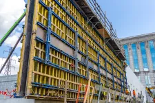 Thumbnail for Large vertical concrete formwork with ladders and scaffolding at an urban construction site on a clear day.