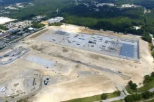 Thumbnail for Aerial view of a large construction site with cleared land and early building foundations surrounded by trees and roads.