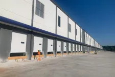Thumbnail for Long row of loading dock doors on a large white warehouse building under clear blue sky.