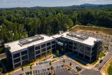 Thumbnail for Modern three-story office building surrounded by trees with large parking lot and clear blue sky