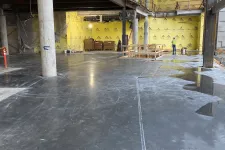 Thumbnail for Interior construction site with polished concrete floor, yellow insulation walls, and worker in safety gear.