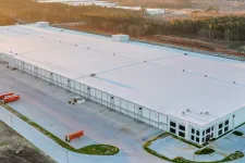 Thumbnail for Aerial view of a large white warehouse building with loading docks and trucks at sunset.