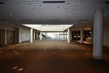 Thumbnail for Spacious empty conference hall with patterned carpet, pillars, escalator, and large glass entrance doors.