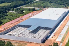 Thumbnail for Aerial view of a large warehouse under construction with steel framework and surrounding green landscape.