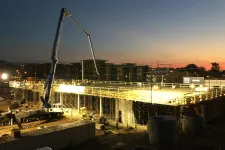 Thumbnail for Nighttime construction site with workers and machinery building a large concrete structure under bright lights.