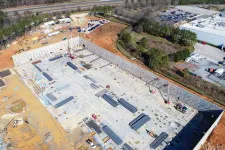 Thumbnail for Aerial view of a large construction site with steel beams and concrete foundation near a forested area.