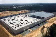 Thumbnail for Aerial view of large warehouse under construction with steel framework and concrete walls in a clearing.