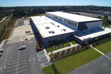 Thumbnail for Aerial view of Third Rail Studios building with parking lot, greenery, and city skyline in the distance on a clear day