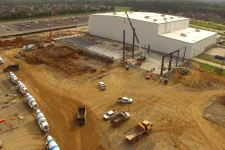 Thumbnail for Aerial view of a construction site with vehicles, cranes, and a large warehouse building under construction.