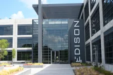 Thumbnail for Modern Edison building entrance with large glass windows and vertical Edison sign on black panel under blue sky.