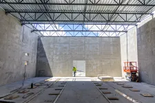 Thumbnail for Construction worker inside a large unfinished building with concrete walls and exposed metal roof beams under daylight.