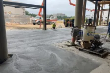 Thumbnail for Construction site with freshly poured concrete floor and workers operating machinery under steel beams.
