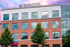 Thumbnail for Modern brick office building with large windows and Spaces logo under a colorful sunset sky.