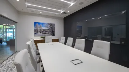 Modern conference room with a long white table, ergonomic chairs, glass walls, and nature artwork on the wall.