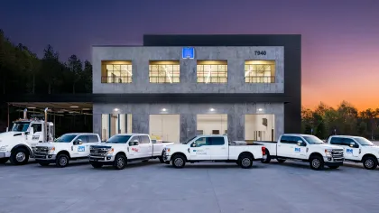 Fleet of white company trucks parked in front of a modern office building during sunset.
