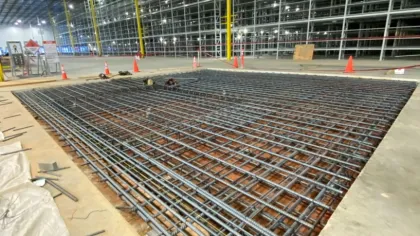 Steel rebar grid foundation in large industrial warehouse under construction with safety cones around.