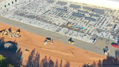 Aerial view of a large construction site with a concrete foundation and construction equipment on red soil.
