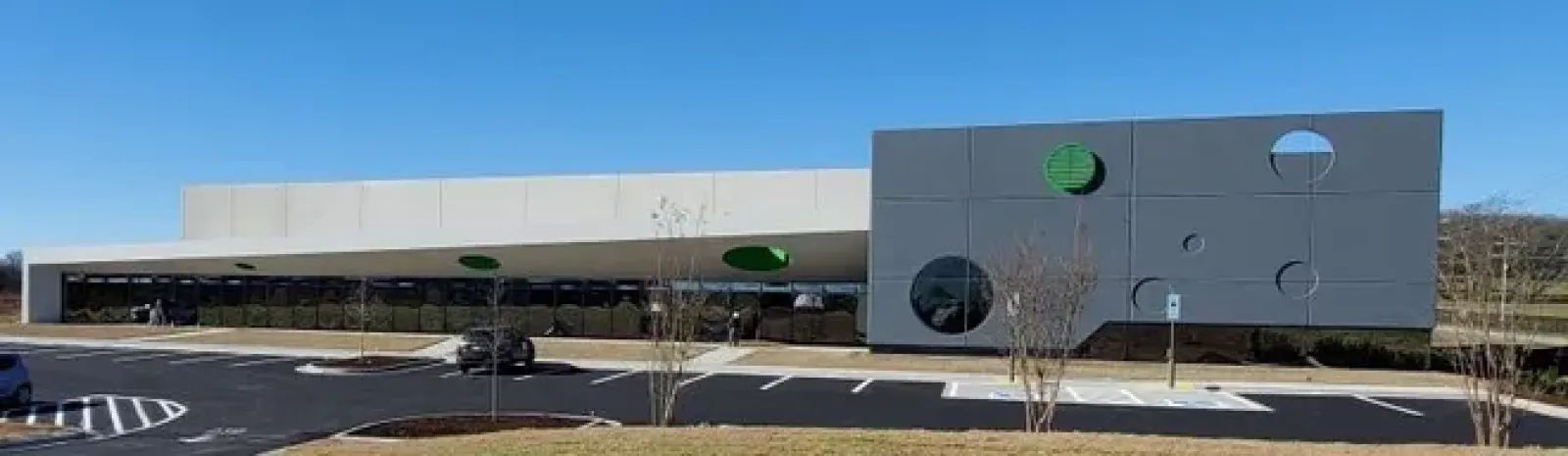 Modern commercial building with gray and white exterior, circular windows, and a clear blue sky background.