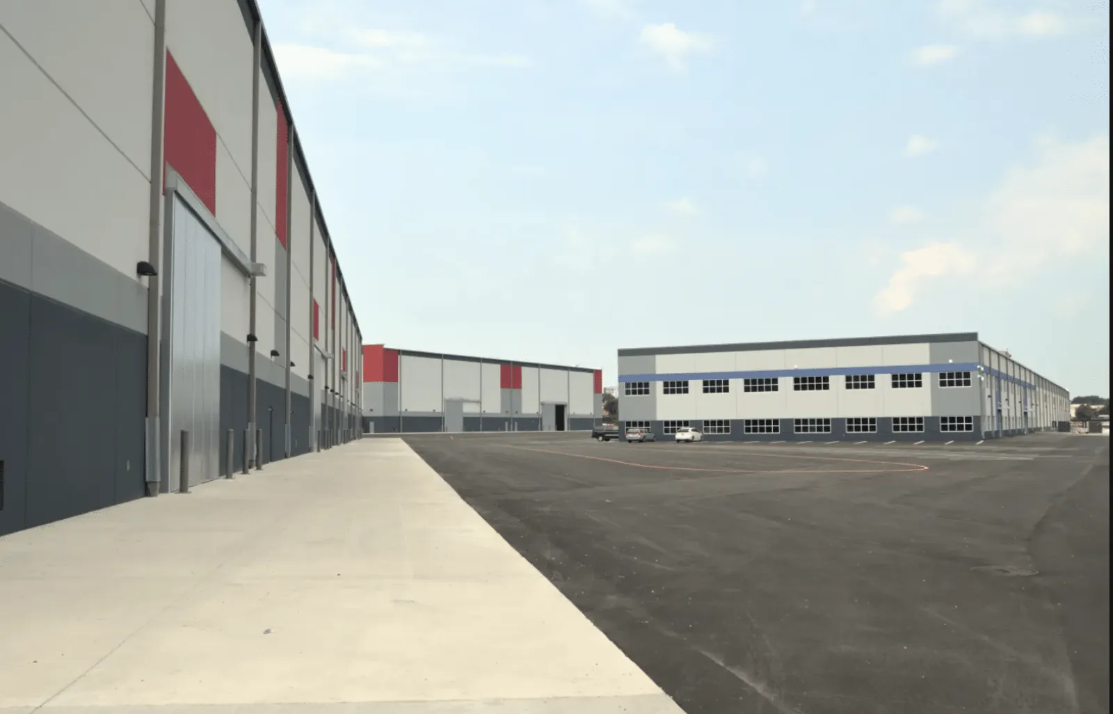Modern industrial warehouses with gray, white, and red exterior walls under a clear sky.