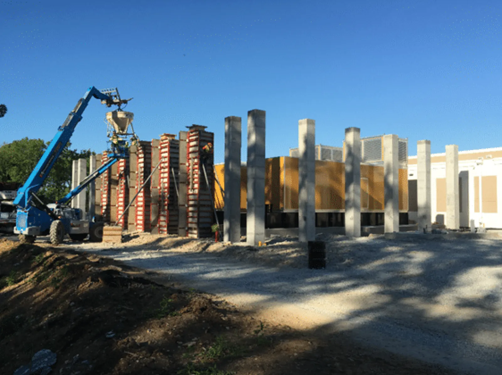 Construction site with concrete pillars and a blue crane lifting building materials under a clear blue sky