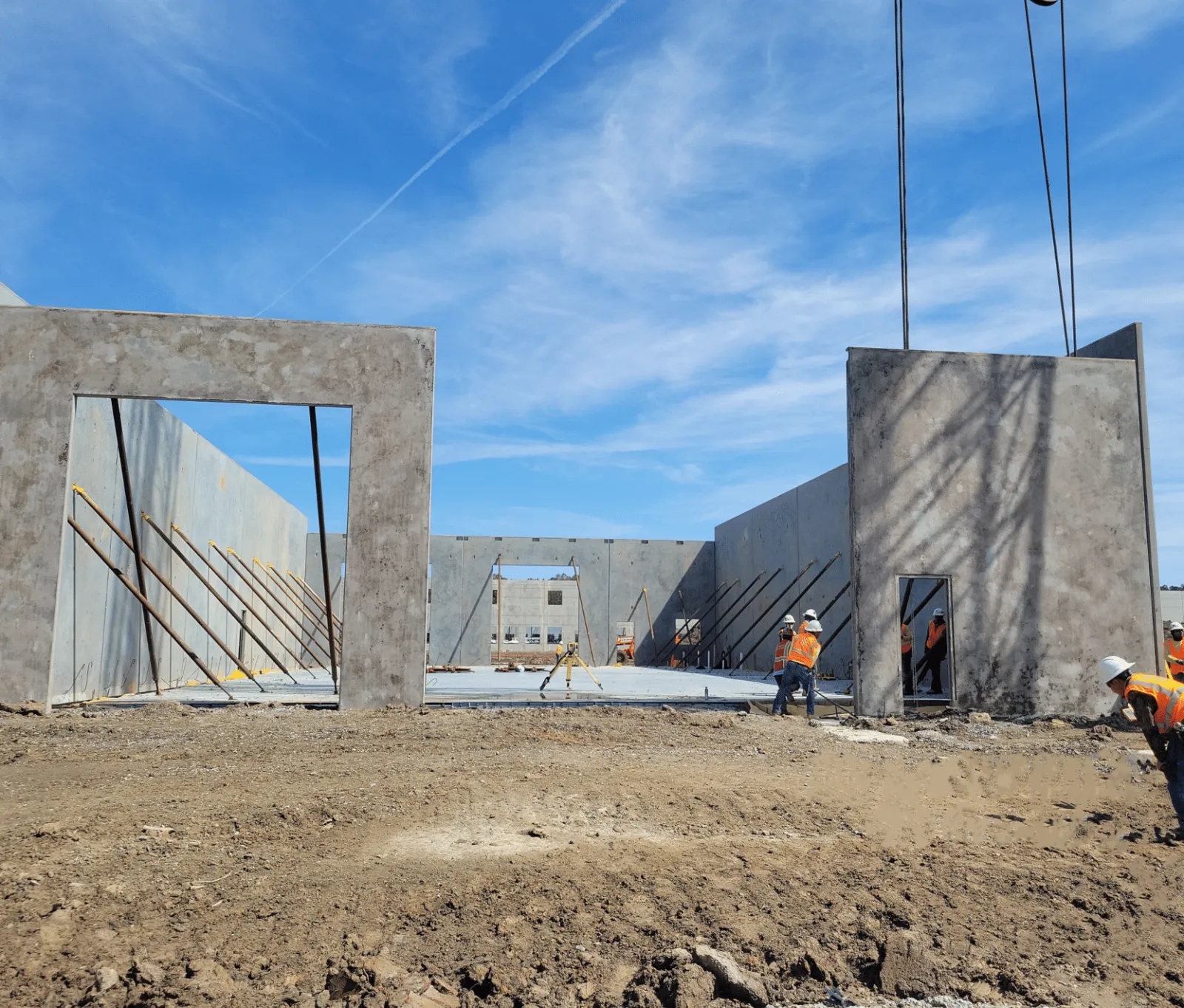 Construction workers building a concrete structure with large walls under a blue sky at a construction site.