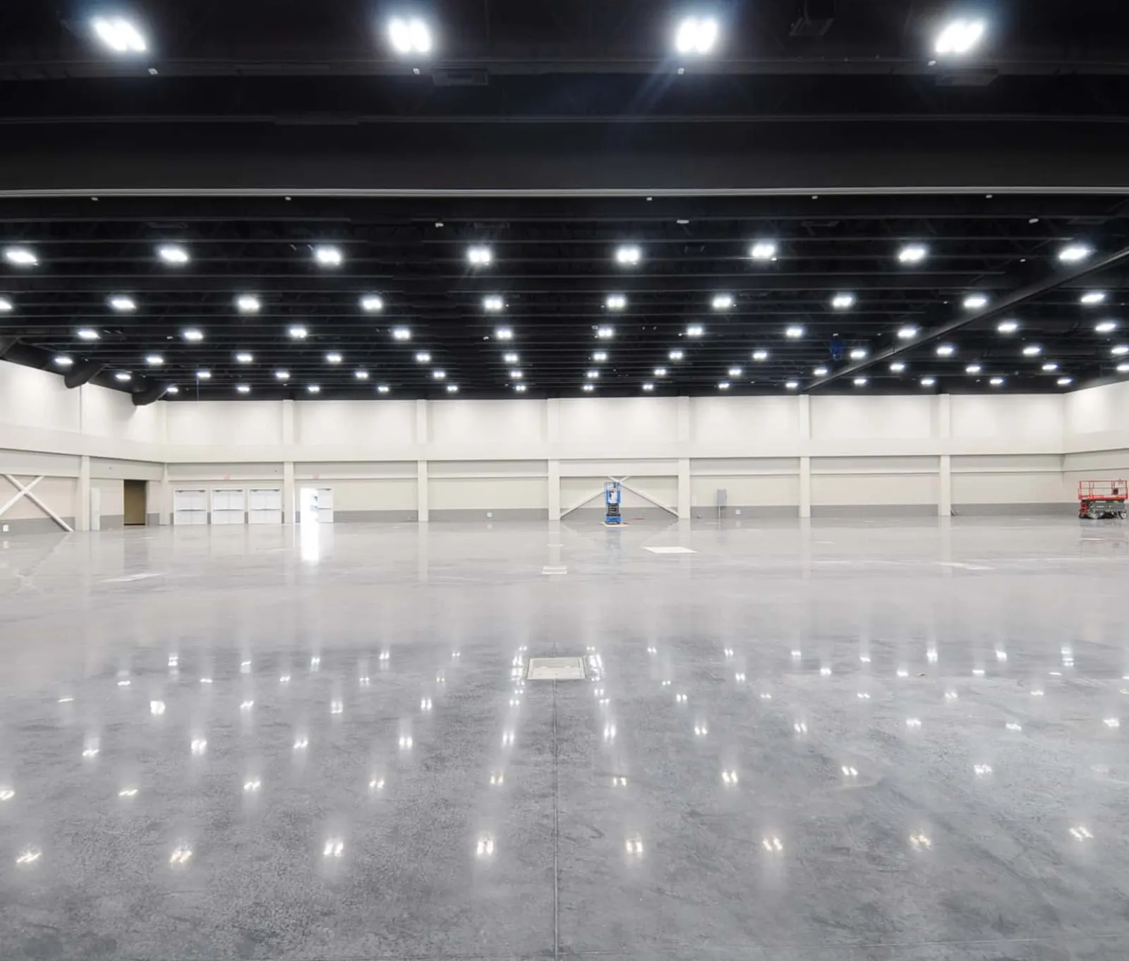 Spacious empty industrial hall with high ceiling and bright overhead lights reflecting on polished concrete floor