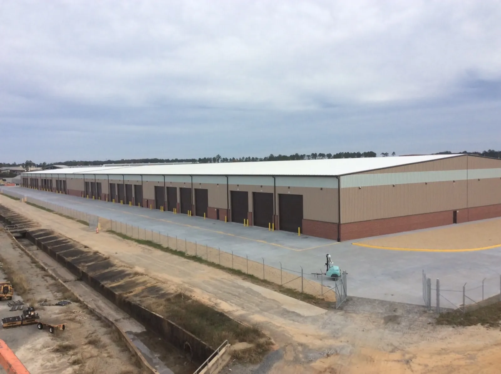 Large industrial warehouse with multiple loading docks and a fenced perimeter under a cloudy sky.