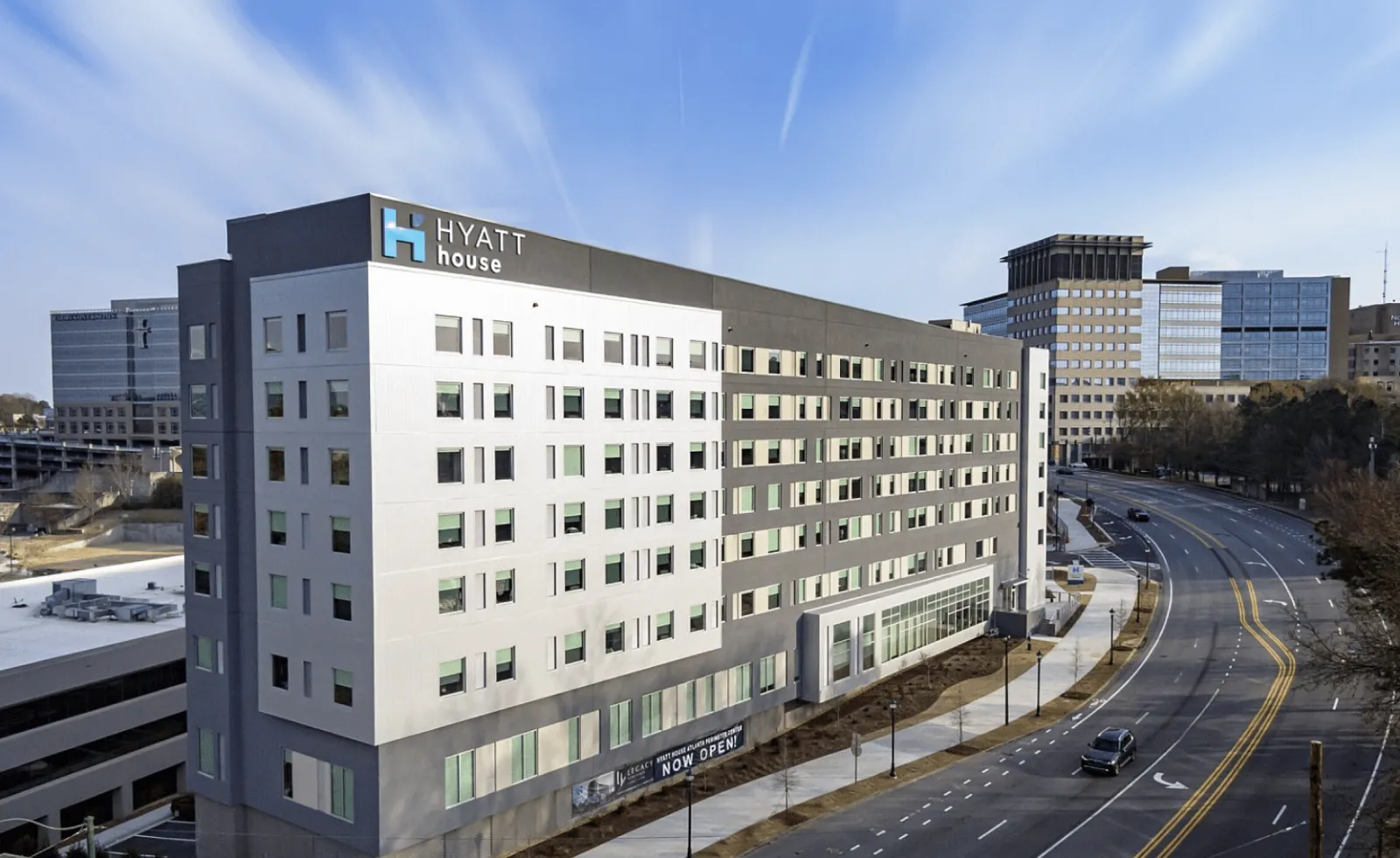 Exterior view of a Hyatt House hotel building on a city street with clear blue sky above.