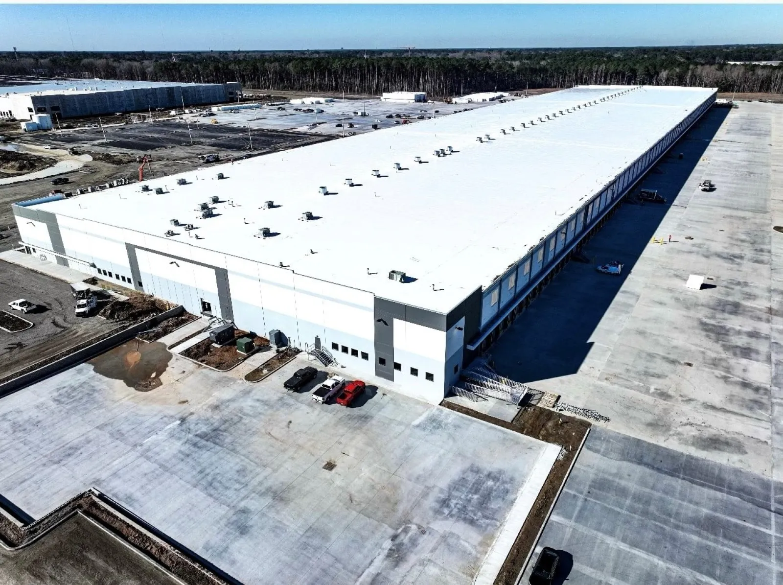 Aerial view of a large white industrial warehouse with surrounding parking and empty concrete space