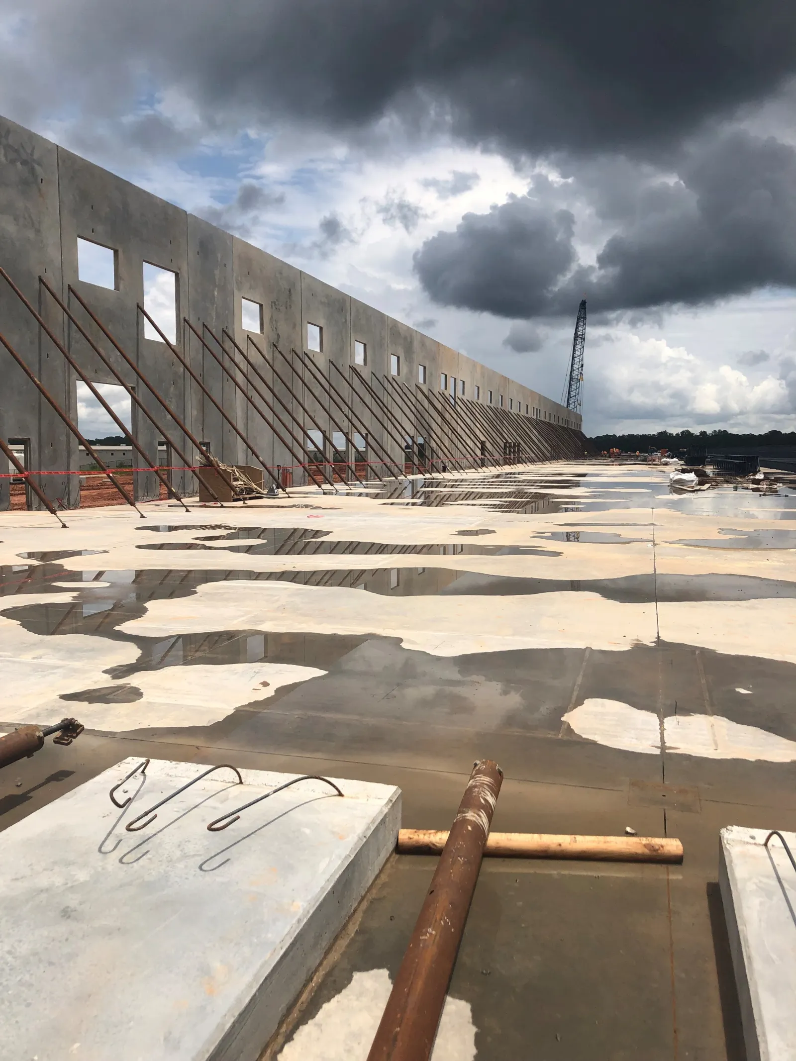 Concrete wall structure under construction with supporting braces and wet concrete floor reflecting cloudy sky.