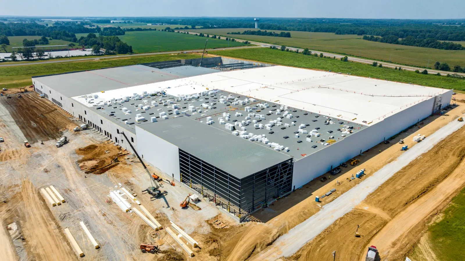 Aerial view of a large warehouse under construction surrounded by farmland and construction equipment.