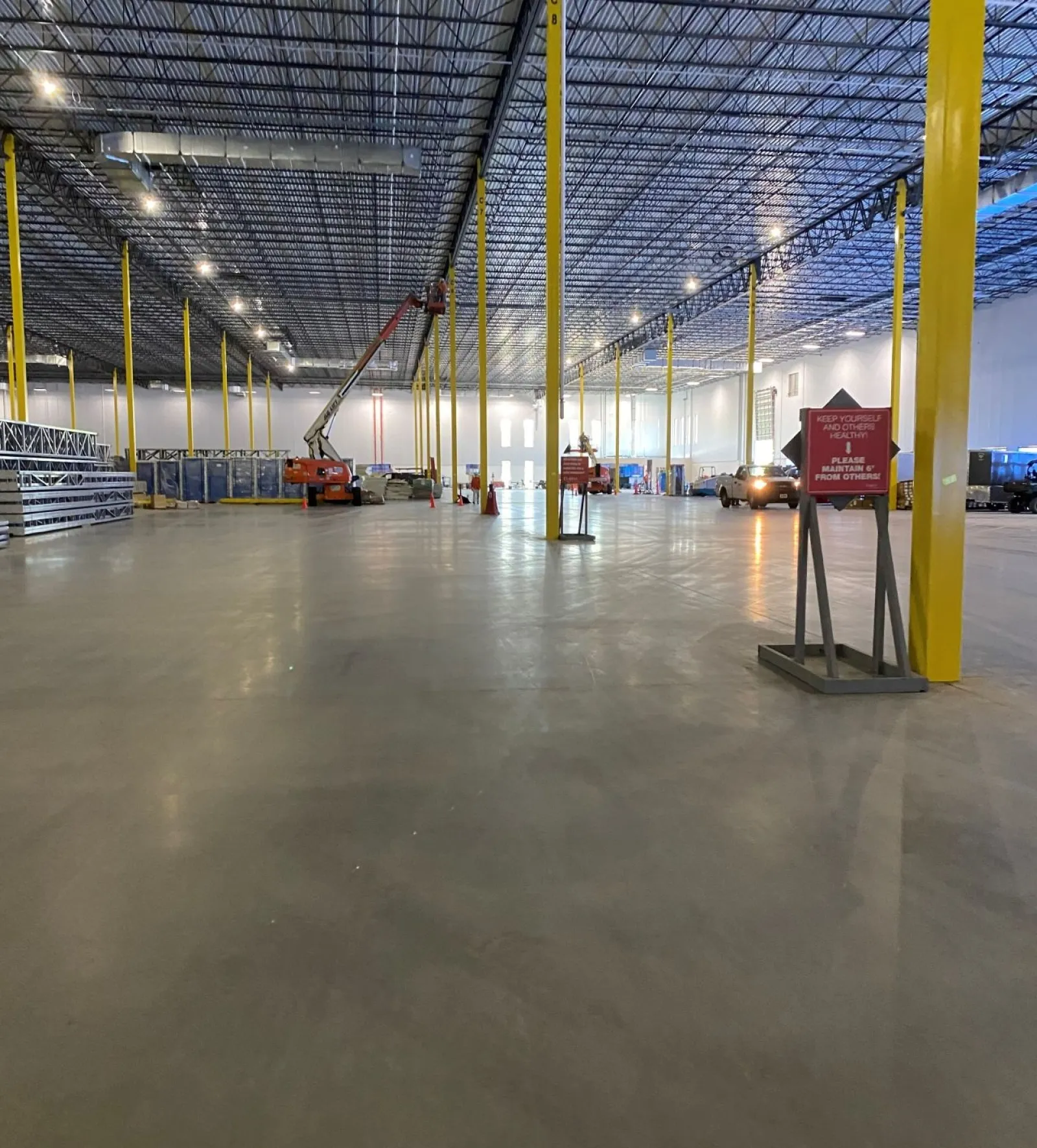 Spacious industrial warehouse interior with yellow support beams, polished concrete floor, and construction equipment.