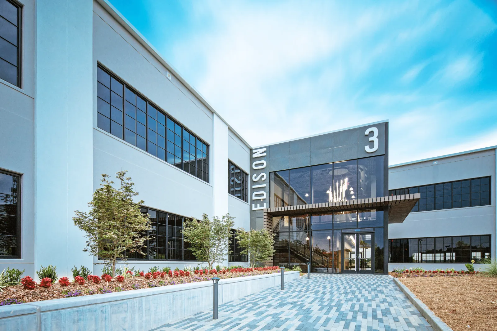 Modern office building with Edison 3 signage, large windows, landscaped entrance, and blue sky background.