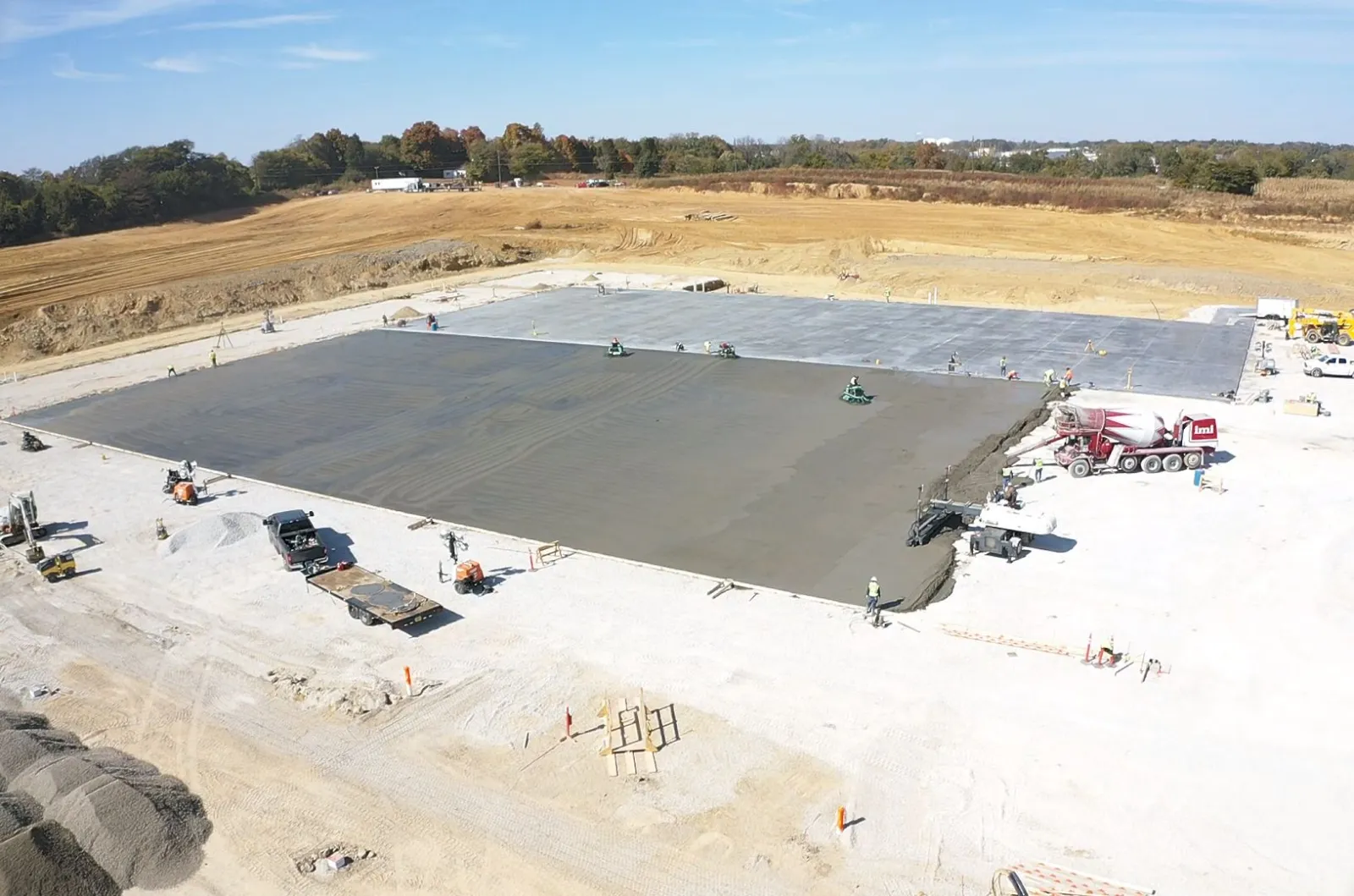 Large construction site with workers and machinery pouring and smoothing concrete foundation slab.