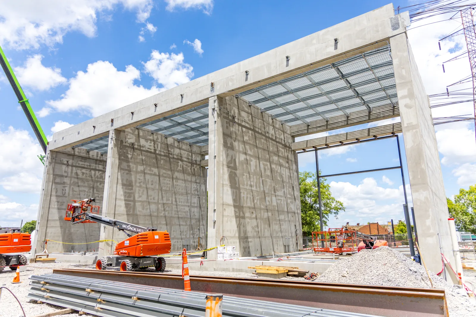 Concrete structure under construction with heavy machinery and steel beams on a sunny day with blue sky.